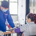 A nurse performs a blood pressure check on a patient in a healthcare setting, emphasizing safety and care.
