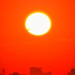 A dramatic red sunset casting vibrant light over the silhouette of a city skyline.