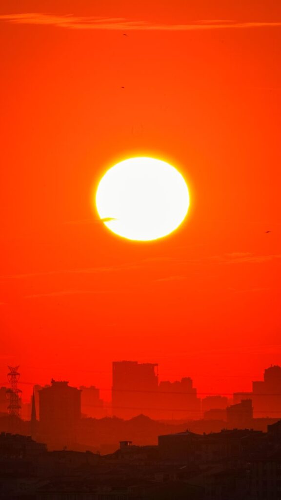 A dramatic red sunset casting vibrant light over the silhouette of a city skyline.