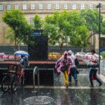 People walking on a wet city sidewalk during a rainstorm, carrying umbrellas and wearing ponchos.