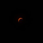A dramatic view of a solar eclipse, showcasing an orange crescent against a dark sky.