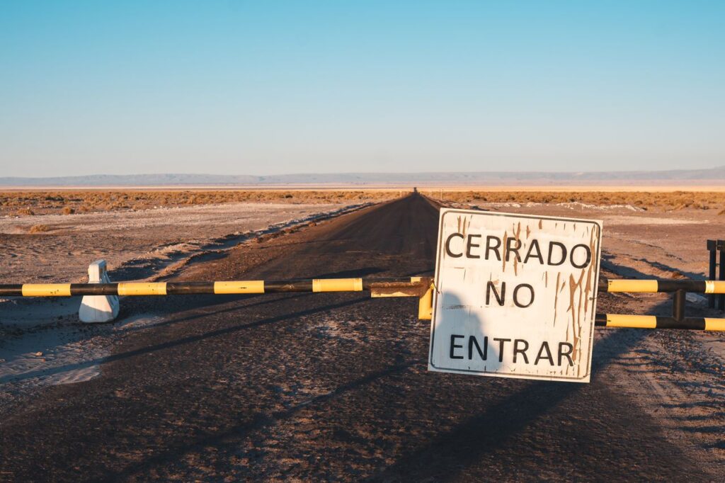 A desert road closed with a sign 'Cerrado No Entrar' at sunset, implying restricted access.