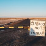 A desert road closed with a sign 'Cerrado No Entrar' at sunset, implying restricted access.