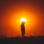 Person silhouetted against a vivid sunset sky in natural landscape.