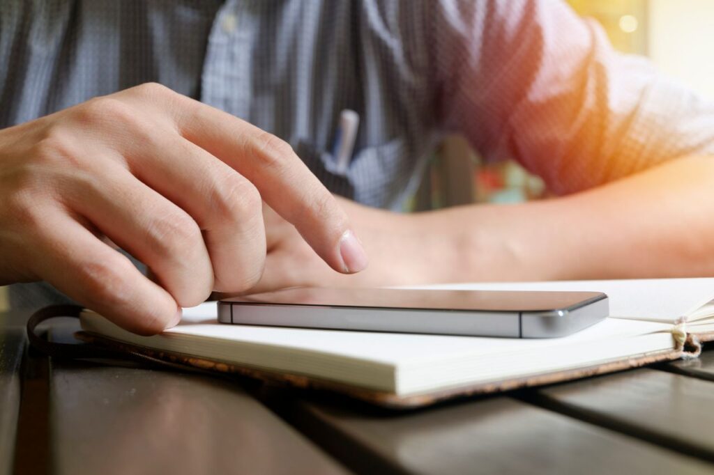A close-up view of a hand interacting with a smartphone and notebook on a desk.