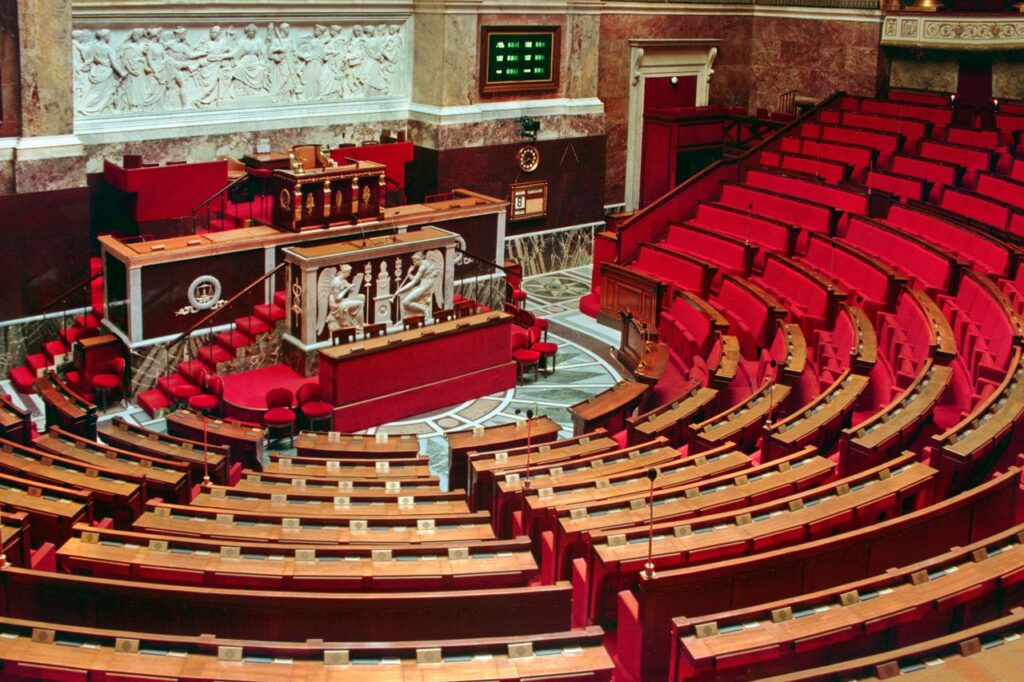 Bright and elegant view of the French National Assembly's rich interior with red seats and ornate decor.