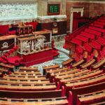 Bright and elegant view of the French National Assembly's rich interior with red seats and ornate decor.