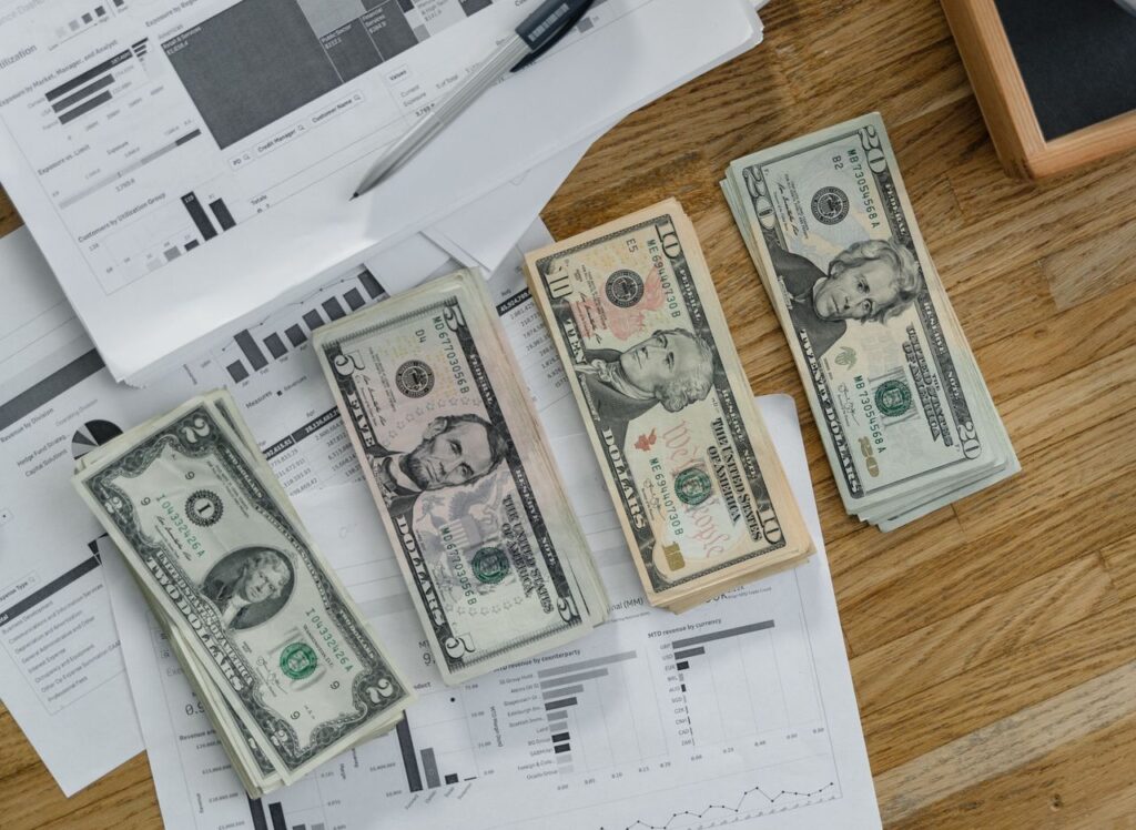 Stacks of US Dollar banknotes placed over financial documents and reports on a desk.