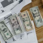 Stacks of US Dollar banknotes placed over financial documents and reports on a desk.
